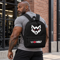 AI-generated original adult tattooed male bodybuilder wearing W8WOLF Bold Wolf Backpack Black in an urban gym setting. Actual black backpack top handle zippers large white wolf red eyes and lower original white wolf red barbell8 WOLF pocket print retained. Clothing styling only.