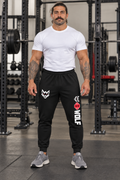 AI-generated original adult tattooed male powerlifter wearing W8WOLF Mens Bold Leg Joggers Black in an urban gym. Actual black elastic waist cuffed construction right thigh white wolf red eyes and left vertical original wolf red barbell8 WOLF artwork retained. Tee and shoes styling only.