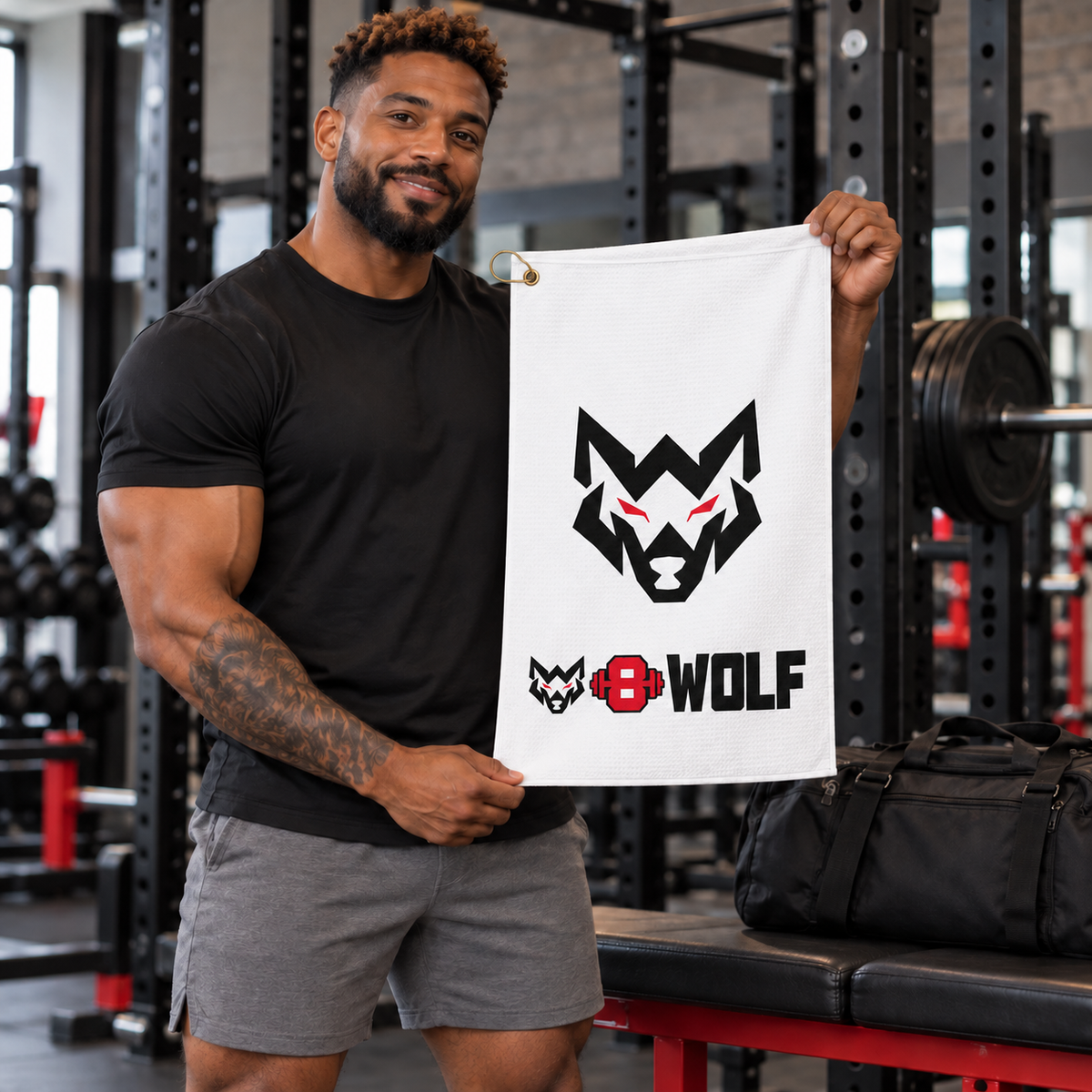 AI-generated original adult tattooed male bodybuilder displaying W8WOLF Signature Wolf Clip Towel White in an urban gym. Actual white microfiber towel original black wolf red eyes and lower wordmark retained; gold grommet ring at top left matches supplier. Clothing and bag styling only.