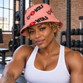 AI-generated original adult tattooed female bodybuilder in an urban gym wearing the Coral side of W8WOLF Coral and Electric Lime Reversible Bucket Hat with original diagonal wolf, red barbell 8 and WOLF pattern. All supplier outside and distinct reverse views retained. White training tank is styling only.