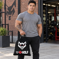 AI-generated original adult tattooed male bodybuilder carrying W8WOLF Bold Wolf Drawstring Bag Black in a fictional urban gym setting. Actual black drawcord bag large white wolf red eyes and lower original white wolf red barbell8 WOLF design retained. Clothing styling only.