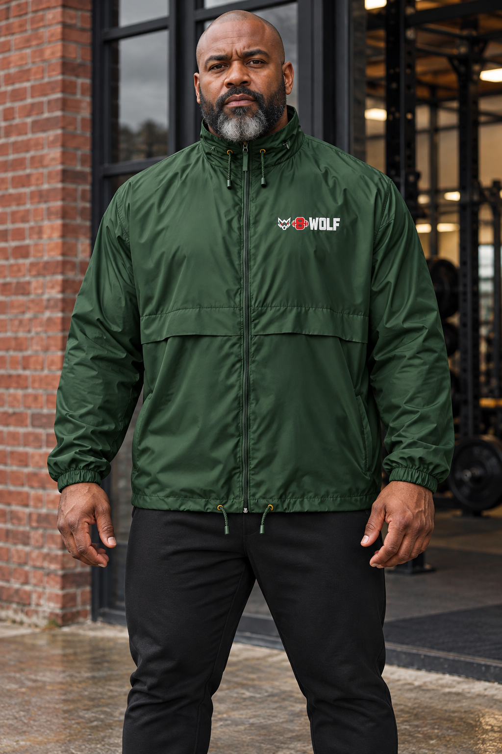 AI-generated original adult male strongman wearing Forest Green W8WOLF Essentials Windbreaker at an urban gym entrance. Actual nylon construction and small original white wolf red barbell8 WOLF left chest mark retained. Black joggers styling only; other color supplier images retained.