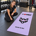 AI-generated original adult tattooed female bodybuilder beside W8WOLF Bold Wolf Yoga Mat Lavender in an urban gym. Actual long lavender mat original wordmark large black wolf red eyes and UNLEASH THE WOLF design retained and fully visible. Clothing styling only.