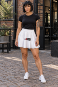 AI-generated original adult tattooed female strength athlete wearing W8WOLF Essentials Skater Skirt in an urban gym courtyard. White flared construction and original front wolf red barbell8 WOLF artwork retained with natural folds. Black tee and shoes styling only.