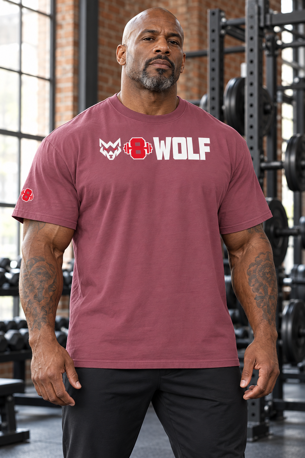 AI-generated original adult tattooed male bodybuilder wearing W8WOLF Bold Logo Heavyweight Tee Brick in an urban gym. Actual dusty berry cotton cut original white wolf red eyes red barbell8 WOLF upper chest and right sleeve barbell retained. Pants styling only.