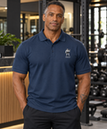 AI-generated original adult tattooed male bodybuilder wearing W8WOLF Iron Curl Signature Polo Navy at an urban gym. Actual navy polo small white embroidered lifting wolf red eyes and W8WOLF below on left chest retained. Plain sleeves match current garment. Pants styling only.