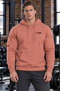AI-generated original adult male bodybuilder wearing W8WOLF Signature Hoodie Dusty Rose in an urban gym. Actual dusty salmon pullover kangaroo pocket tiny left chest black wolf red eyes red barbell8 WOLF and right sleeve wolf retained. Pants styling only.