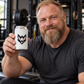 AI-generated original adult strongman holding W8WOLF Wolf Emblem Can Cooler Regular 12 oz in an urban strength gym. Actual white neoprene sleeve black seam and original black wolf red eyes artwork retained. Unbranded can and clothing styling only.